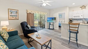 A living room with a blue sofa, a wooden coffee table, a black armchair, and a kitchen area with white cabinets and a microwave. - Royal Poste Unit 3203 (Sunset Beach)