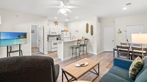 A modern living room with a TV, sofa, and coffee table. There is a kitchen area with a dining table and chairs. - Royal Poste Unit 3203 (Sunset Beach)