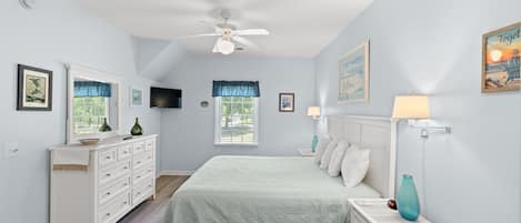 A bedroom with a bed, dresser, nightstand, ceiling fan, and artwork on the walls.