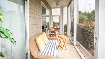 Ein überdachter Balkon mit Rattan-Sofa, einem kleinen Tisch und einem Stuhl.