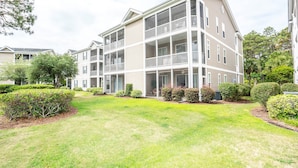 A multi-story residential building with balconies, a well-maintained lawn, and mature landscaping. - Sandpiper 2A (Sunset Beach)