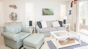 A living room with a light blue sofa, a striped sofa, a glass coffee table, and decorative wall art. - Sandpiper 2A (Sunset Beach)