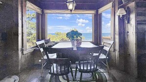 A dining area with a table and chairs, a hanging light fixture, and a view of the ocean. - Seacoast Sanctuary (Cape Neddick)