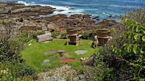 A coastal view with two wooden structures, a grassy area with stepping stones, and a rocky shoreline. - Seacoast Sanctuary (Cape Neddick)