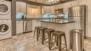 A modern kitchen with stainless steel appliances, a central island with stools, and a built-in washing machine. - Sandhill Flat (Gary)