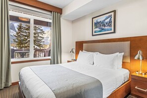 Ein Hotelzimmer mit einem großen Bett, einem hölzernen Kopfteil, einem Nachttisch mit Lampe, einem Fenster mit Vorhängen und einem gerahmten Bild an der Wand.