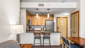 A compact kitchen with wooden cabinets, a stainless steel refrigerator, and a small island with bar stools. - Serene 1BR Rockies Retreat w/ BBQ, Gym & Hot Tub (Canmore)