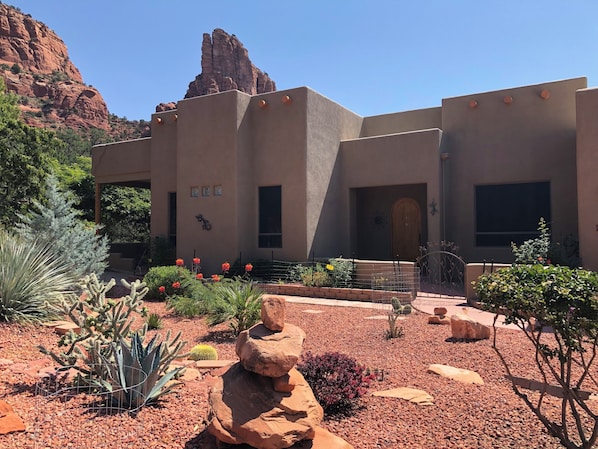 A building with a desert garden, including cacti and flowering plants, and a prominent rock formation in the background. - Sedona Quail Haven (Sedona)