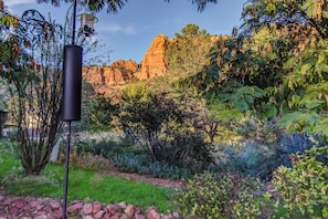 A garden with a variety of plants and trees, a stone pathway, and a rocky mountain backdrop.