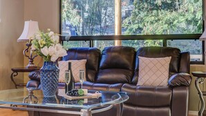 Ein Ledersofa mit Kissen, ein Glastisch mit Flasche, Gläsern und Trauben sowie eine Vase mit Blumen.