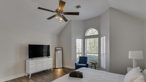 A bedroom with a large bed, a TV, a ceiling fan, a chair, and a window with blinds. - The Prestige Poolside Escape - 5BR w Cinema & Gaming (DeSoto)