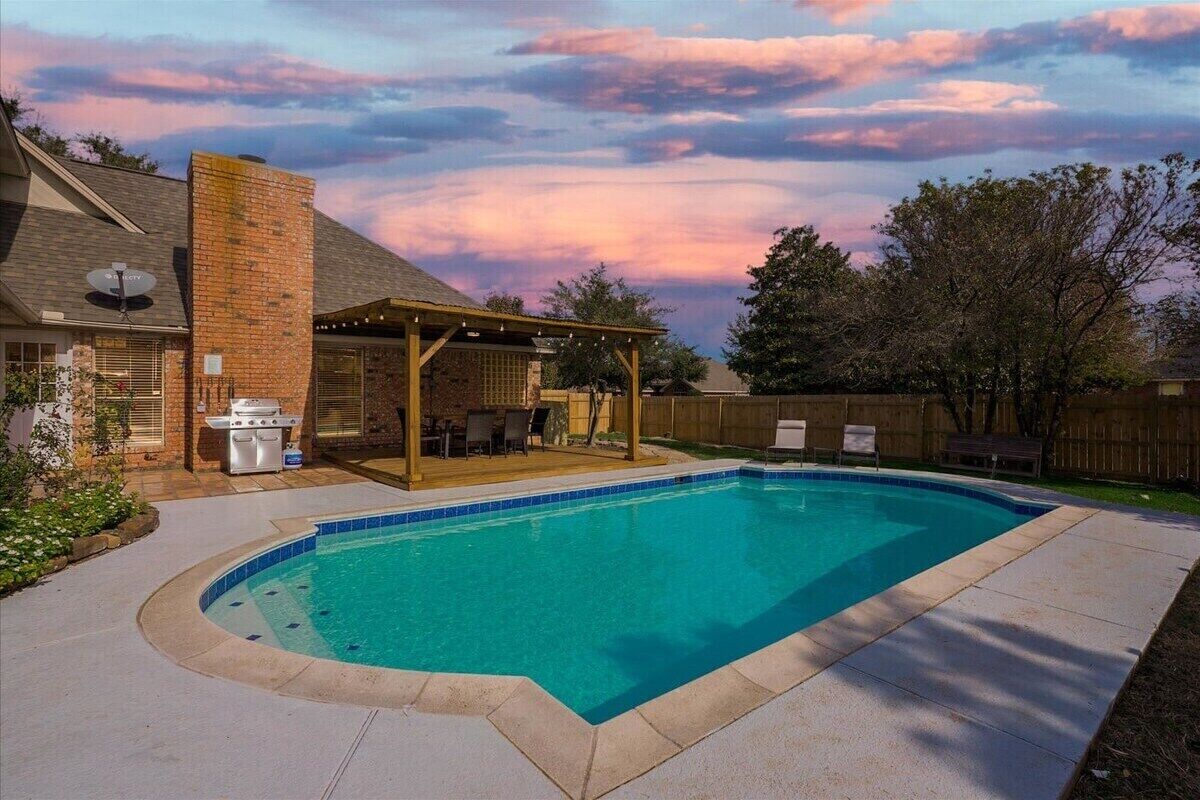 A backyard with a swimming pool, a barbecue area, and a covered patio.