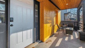 Une véranda couverte avec une porte blanche, des murs en bois et du mobilier d’extérieur.