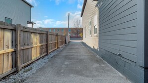 Un étroit chemin de béton bordé de clôtures en bois et de bâtiments dont le revêtement extérieur est de couleur claire.
