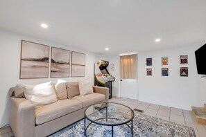 A living room with a beige sofa, a glass coffee table, and a wall-mounted gaming machine. - Stylish Nashville Getaway With Free Parking (Nashville)