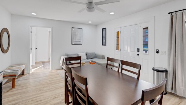 Un espace de repas moderne avec une table et des chaises en bois, un ventilateur de plafond et une vue sur l’extérieur.