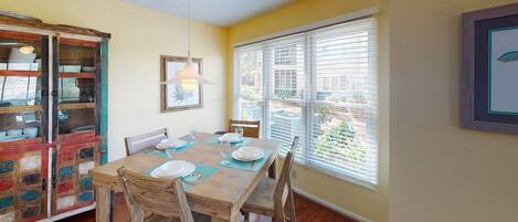 A dining area with a wooden table set for four, chairs, a hanging light fixture, and a window with blinds.