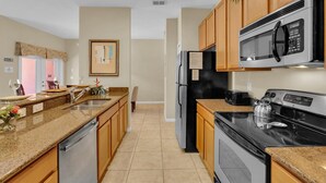 A modern kitchen with granite countertops, stainless steel appliances, wooden cabinets, and a tiled floor. - Cpr8972 (Kissimmee)