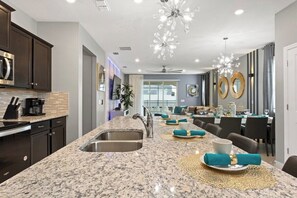 A modern kitchen with granite countertops, stainless steel appliances, and a dining area with a long table set for six. - Ultimate Windsor Island 7BR Pool spa Game Room (Davenport)