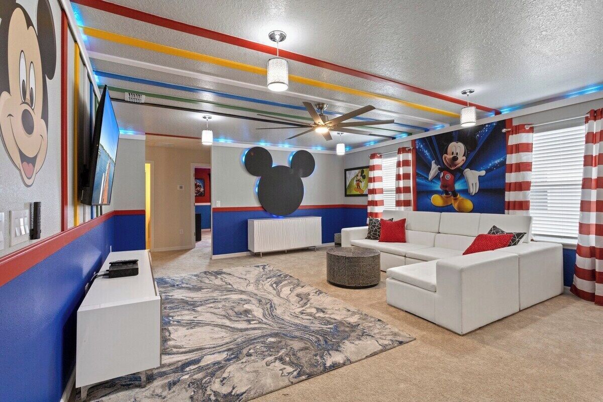 A living room with a white sofa, a large Mickey Mouse mural, and a ceiling fan.