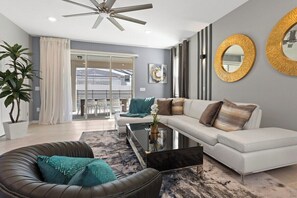 A modern living room with a white sofa, a black leather chair, a glass coffee table, and a ceiling fan. - Ultimate Windsor Island 7BR Pool spa Game Room (Davenport)