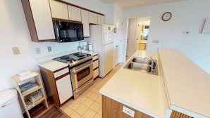 A compact kitchen with a microwave, stove, oven, and a double sink. - River Creek 1 Unit 304 (Sunset Beach)