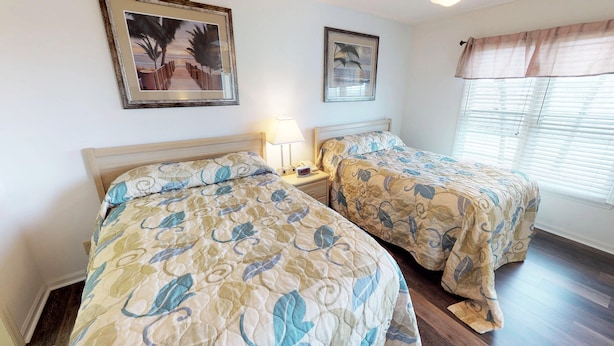 A hotel room with two beds, a nightstand with a lamp, and two framed pictures on the wall. - River Creek 1 Unit 304 (Sunset Beach)