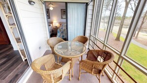 A balcony with wicker chairs and a glass table, overlooking a grassy area. - River Creek 1 Unit 304 (Sunset Beach)