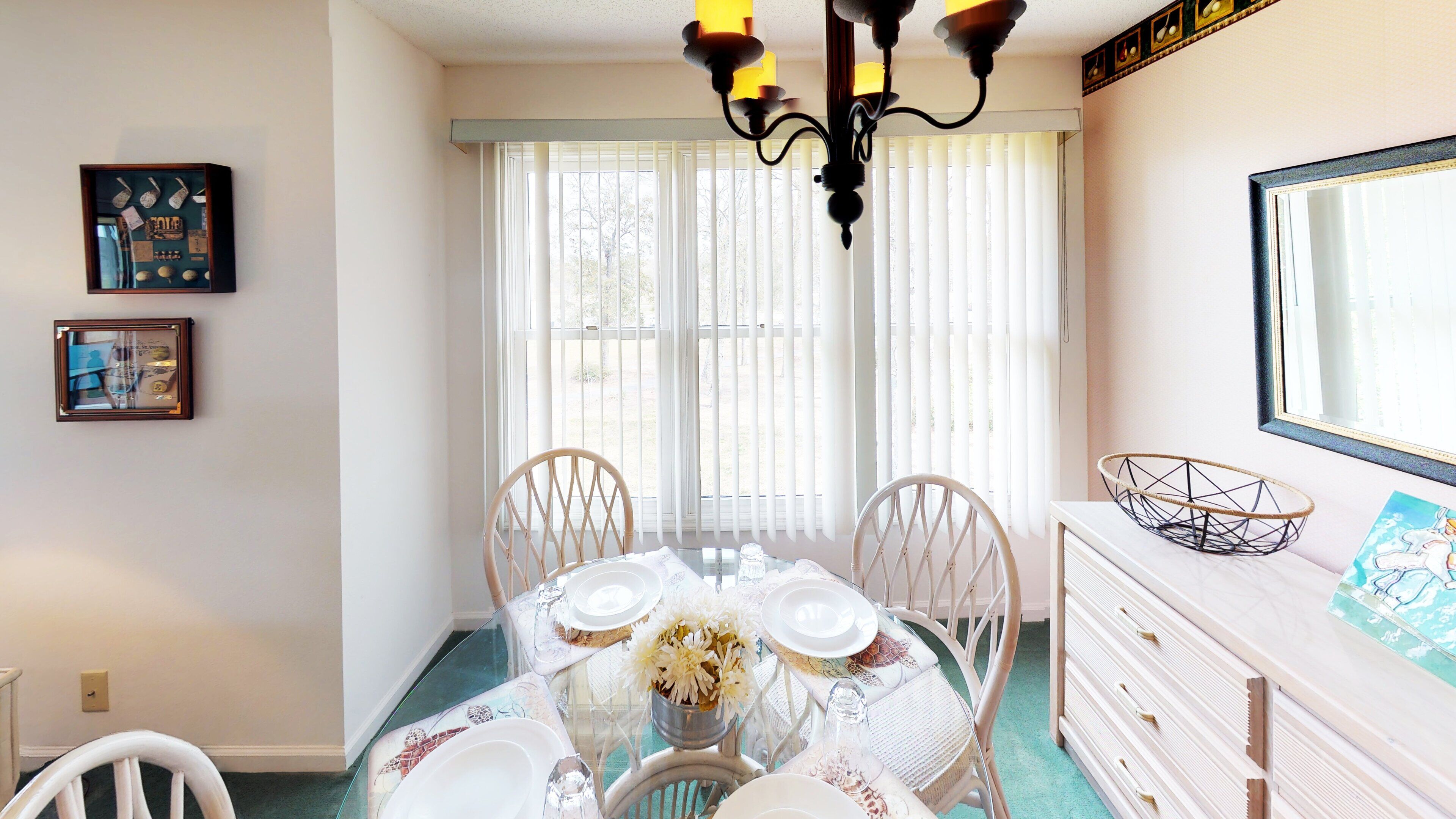 A dining room with a glass table, white chairs, a chandelier, and a dresser with a mirror.