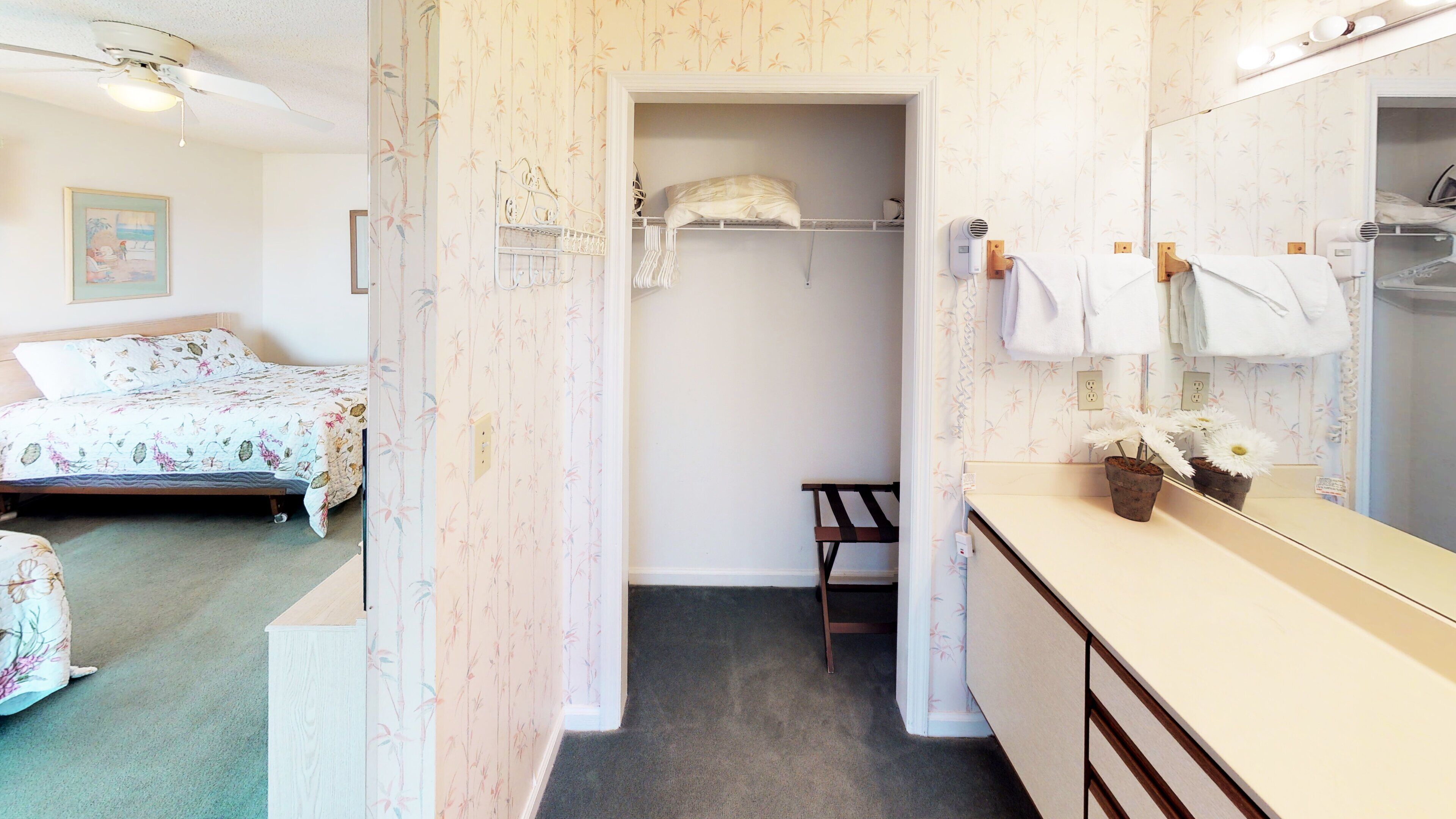 A bedroom with a bed, a small desk, a mirror, and a bathroom with a sink and towel rack.