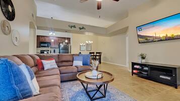 A modern living room with a brown leather sofa, a round coffee table, and a flat-screen TV mounted on the wall.