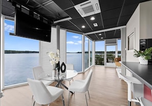 A modern interior with a dining area, kitchen, and large windows overlooking a body of water. - The Glass Mansion (Terrell)