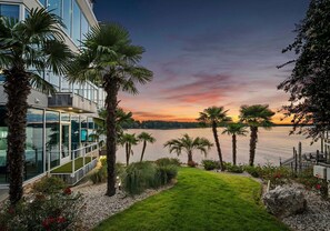 A modern building with glass windows, palm trees, and a view of a lake at sunset. - The Glass Mansion (Terrell)