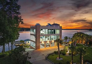 A modern building with a glass facade, a dock, and a view of the water at sunset. - The Glass Mansion (Terrell)