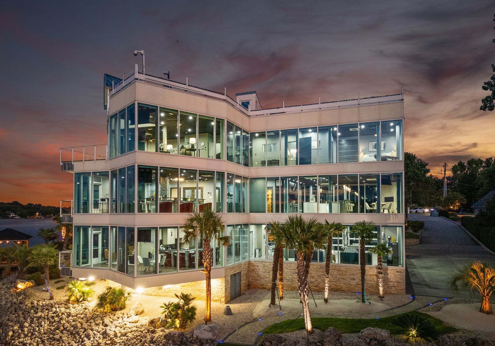 A multi-story building with large glass windows, a flat roof, and a landscaped area with palm trees.