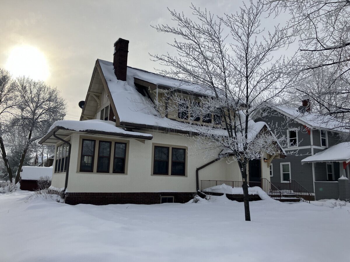 A two-story house with a snow-covered roof and a chimney.