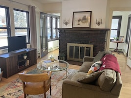 Una sala de estar con chimenea, un sofá, una mesa de centro de cristal y un televisor sobre un mueble de madera.