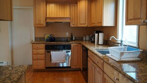 A kitchen with wooden cabinets, a dishwasher, a stove, a sink, and granite countertops. - Short Sands View Y770-g (York Beach)