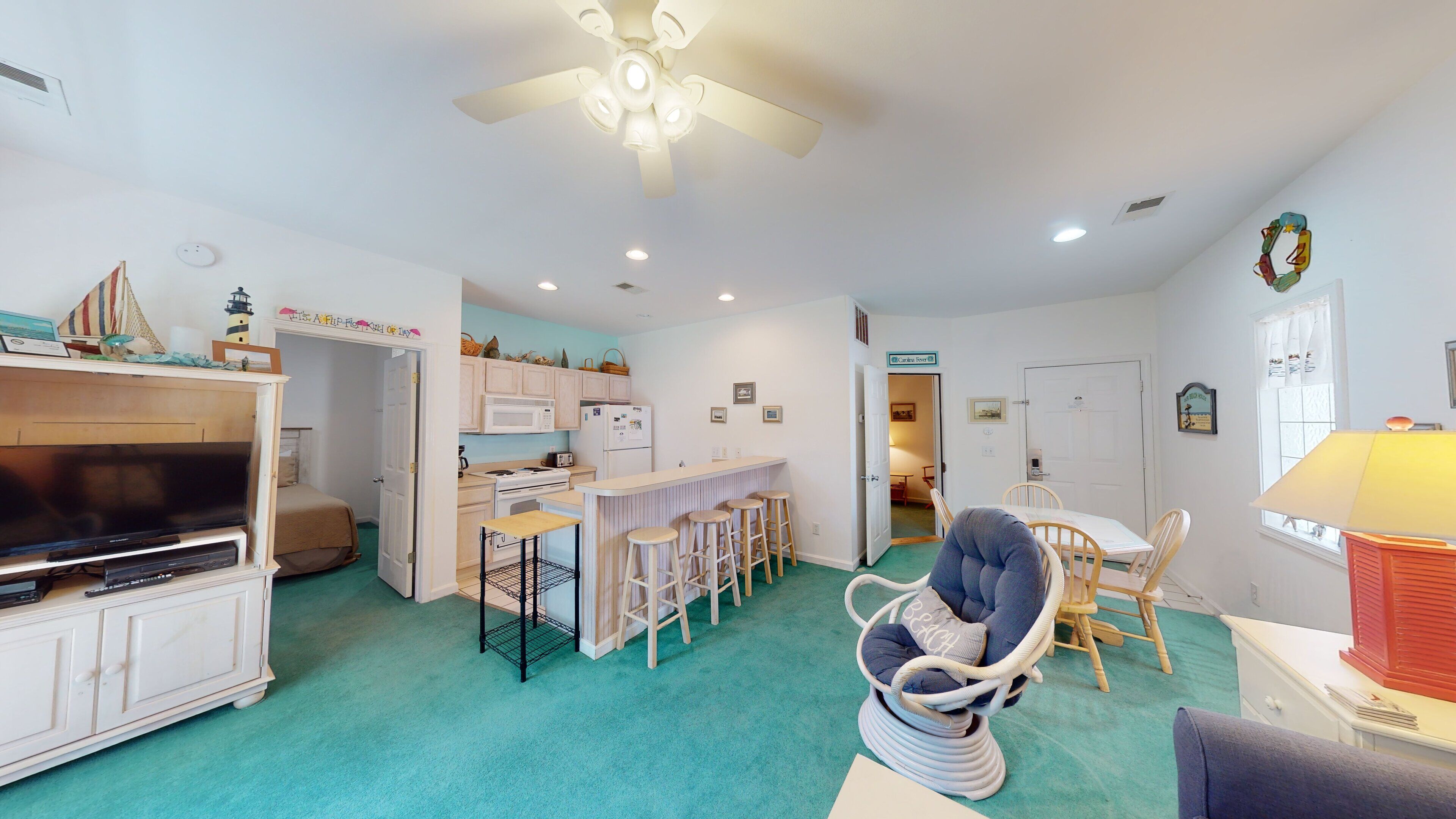 A compact living space with a kitchenette, a dining area, and a seating area with a beach-themed chair.