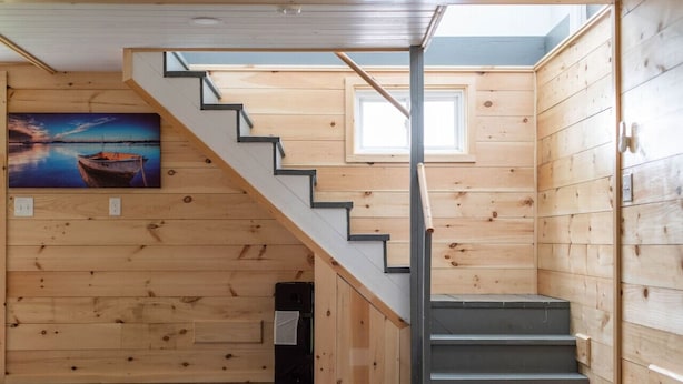Interior de madera con una escalera, un cuadro de un barco y una ventana.