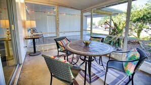 A covered patio with a round table, chairs, and a small table with lamps. - Stylish Retro Vibes Private BBQ & Beach Access (Sarasota)