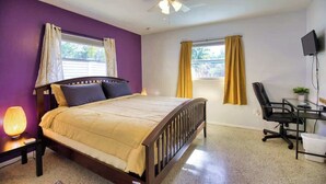 A bedroom with a bed, a desk, a chair, a ceiling fan, and two windows with curtains. - Stylish Retro Vibes Private BBQ & Beach Access (Sarasota)