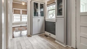 A hallway with a wooden floor, white cabinets with glass doors, a window with a view, and a door. - Stylish 3-bedroom Home in Tulsa (Tulsa)