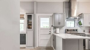 A kitchen with white cabinetry, a central island, a stainless steel range hood, and a window above the sink. - Stylish 3-bedroom Home in Tulsa (Tulsa)