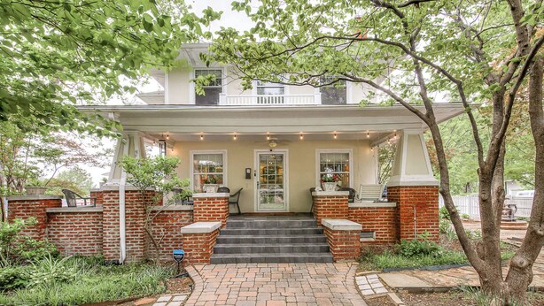 A two-story house with a brick exterior, a front porch, and a small garden area. - Stylish 3-bedroom Home in Tulsa (Tulsa)