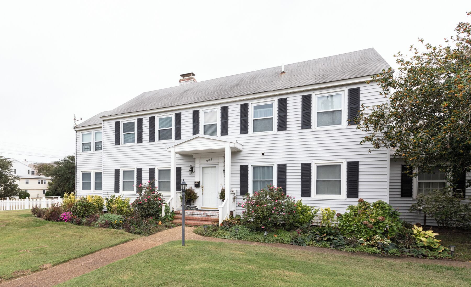 A two-story white house with black shutters, a front porch, and a well-maintained garden.