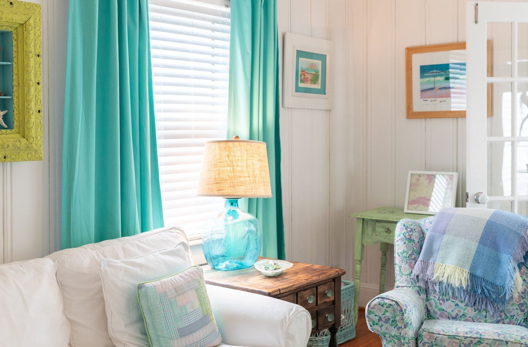 A cozy room with a white sofa, a blue lamp, and a floral armchair.