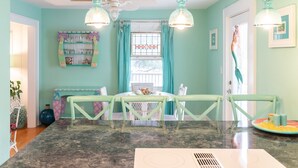 Un espace repas doté d’un comptoir en marbre, de chaises vertes et de luminaires suspendus.