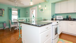 Une cuisine avec des armoires blanches, un four à micro-ondes et une cuisinière. On y trouve une table à manger avec des chaises et un ventilateur de plafond.