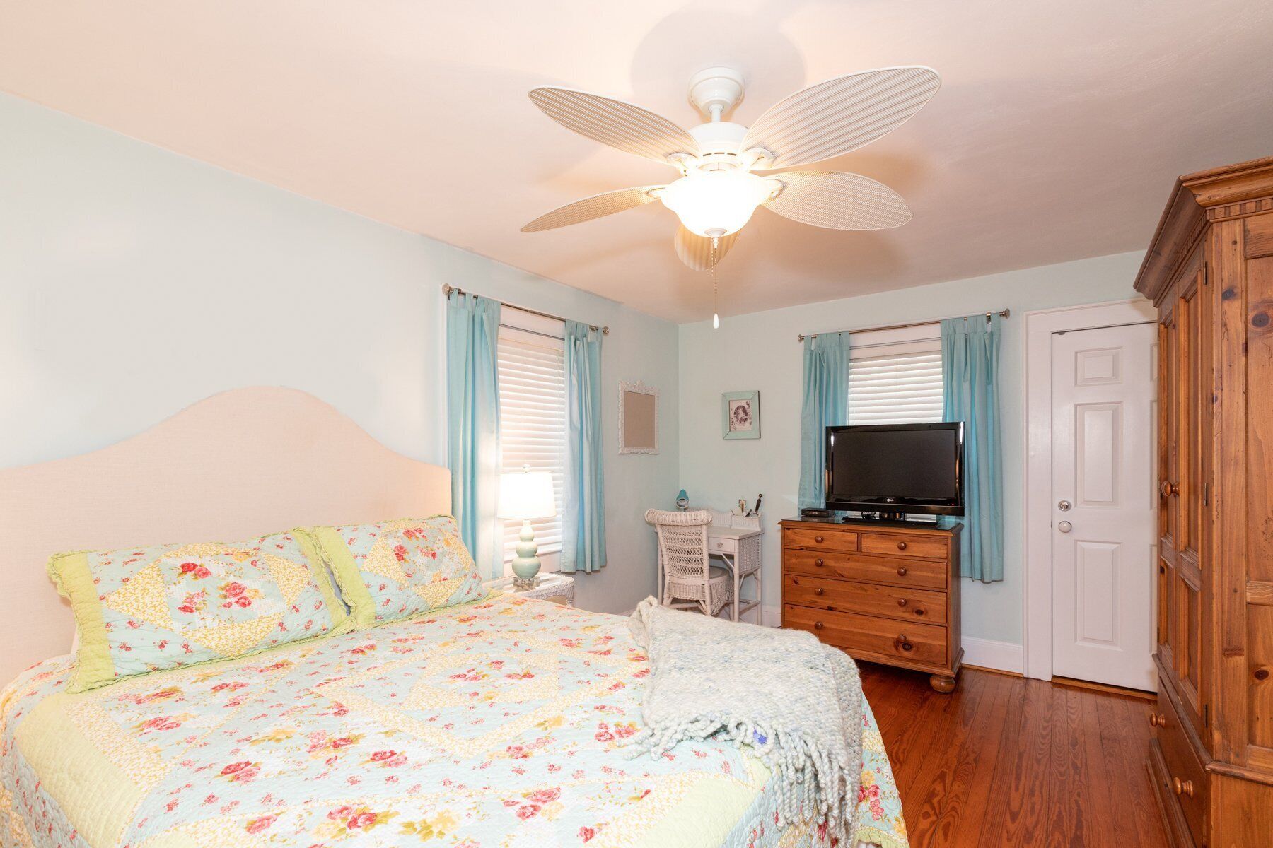 Une chambre à coucher comprenant un lit, une commode, un téléviseur et un ventilateur de plafond.